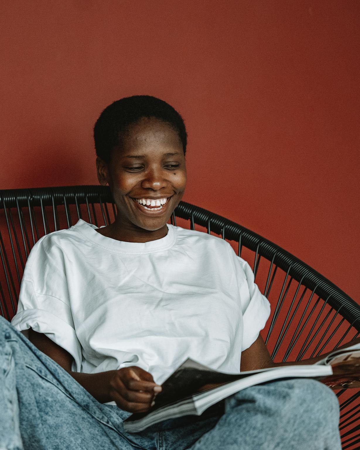 Smiling woman reading a magazine while sitting comfortably in a chair indoors.